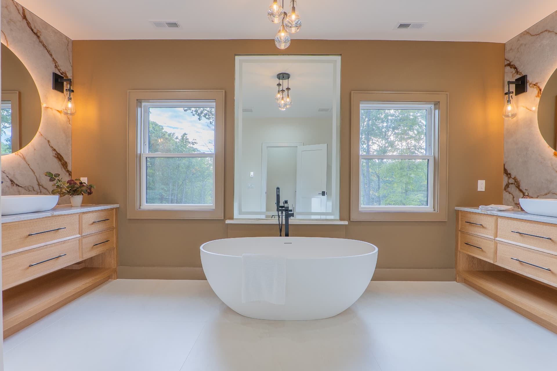 Primary bathroom with freestanding soaking tub, twin white oak vanities and backlit stone mirrors