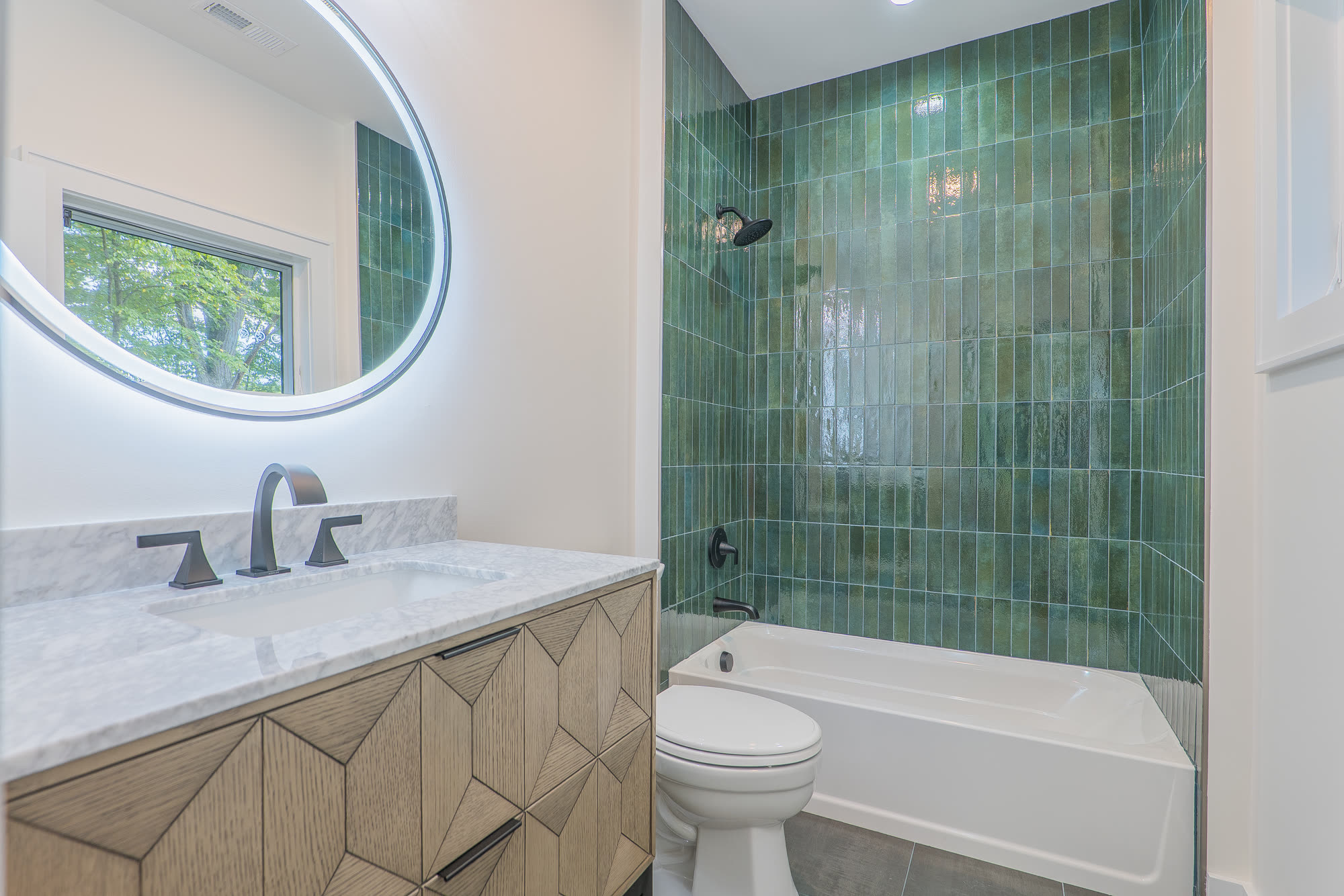 Bath with emerald green tile and round lit mirror