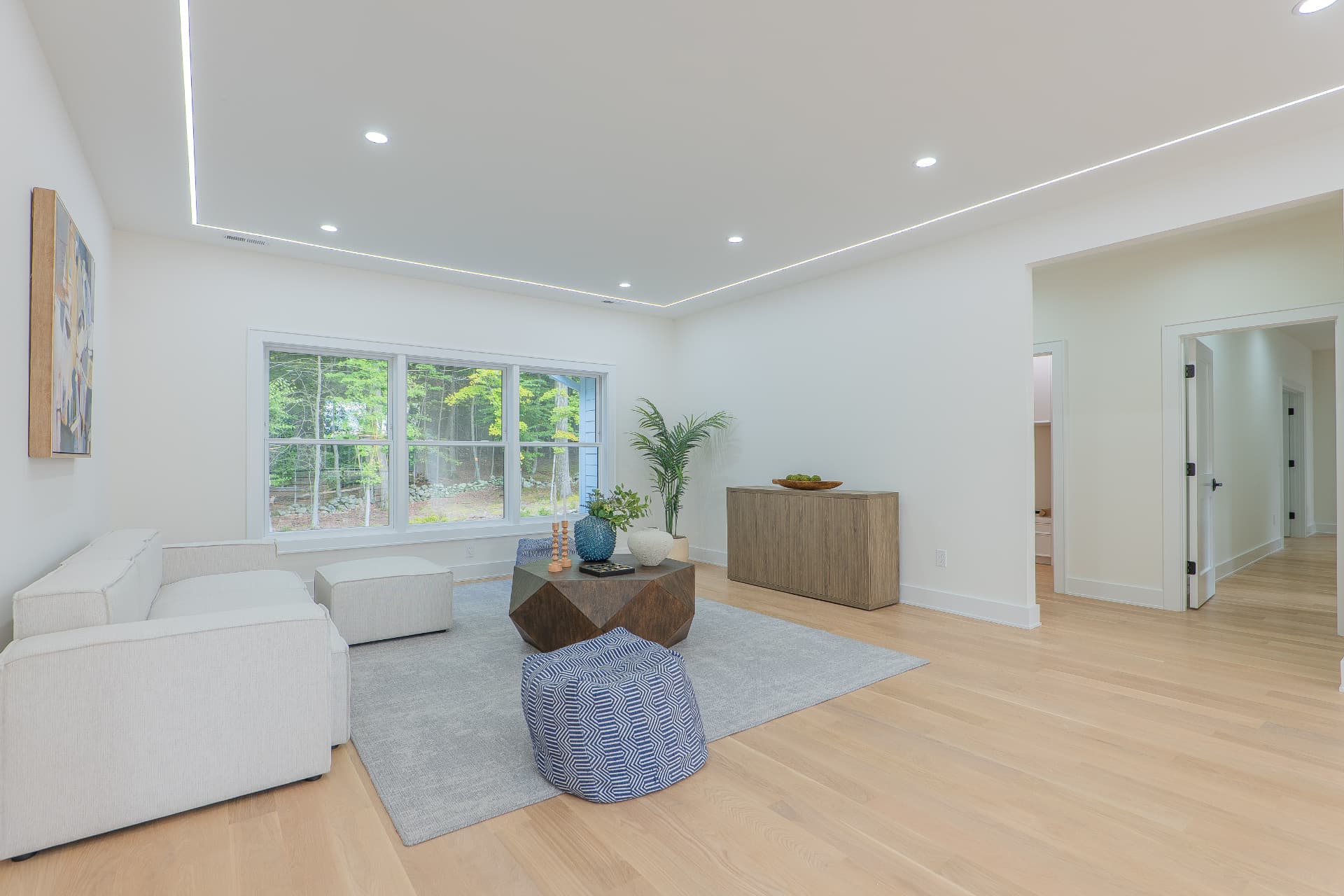 Second-floor loft with white sectionals, cove-lit ceiling and windows to the wooded grounds